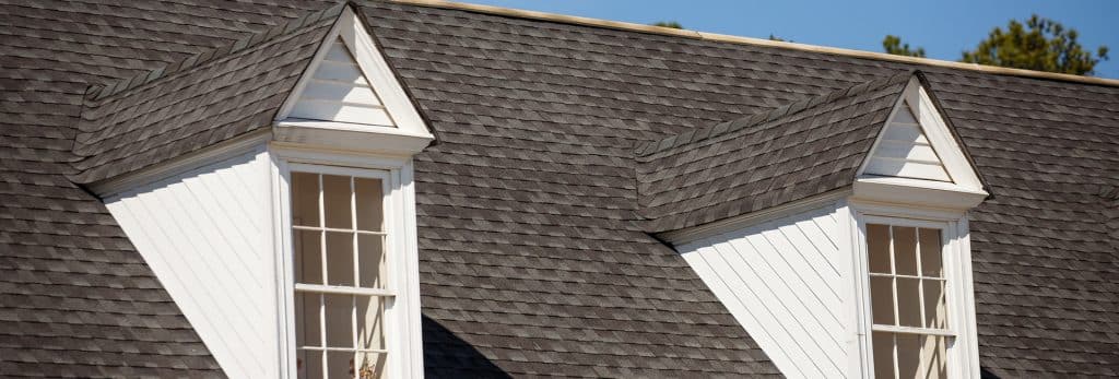 A residential rooftop with architectural asphalt shingles and two dormer windows.