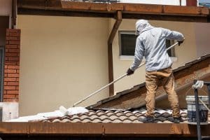 Worker adding undercoat foundation paint onto rooftop with roller as primer at residential building in renovation